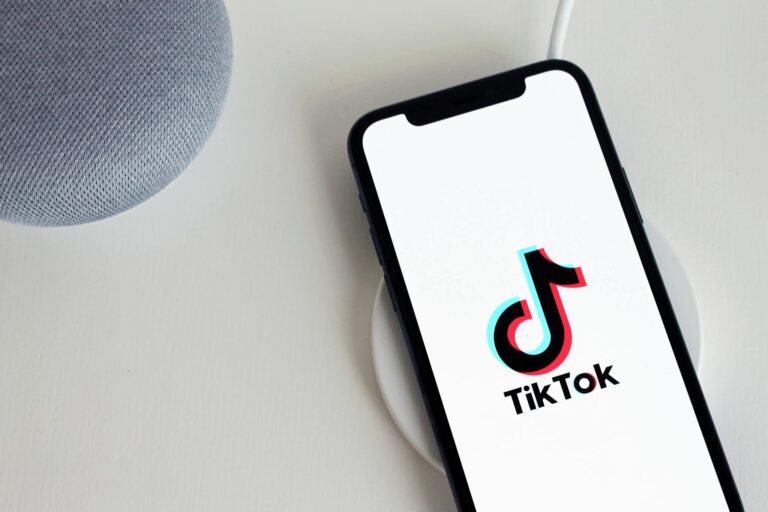 Smartphone displaying TikTok app logo, placed on a wireless charger beside a smart speaker.
